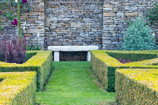 Relaxing white bench by a stone wall in a landscaped garden, with trimmed boxus hedge .