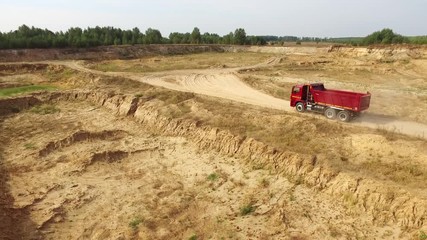 Aerial view the red truck moving on sand track against grey sky and trees on the background. Beautiful view from above.