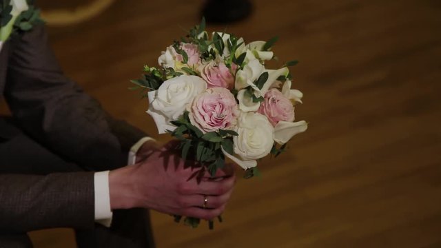 The man is holding a bouquet with lace ribbons in his hand. Tapes develop in the wind. The groom keeps beautiful flowers.