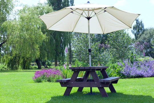 Relaxing setting in a pub garden with umbrella sitting bench next to flowers in bloom, willow trees, al fresco dining in an English countryside on a sunny summer day .