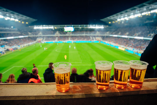 Beers At Soccer Stadium. Football Game In Background