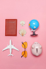 Vacation travel summer weekend sea adventure trip concept. Minimal simple flat lay with plane passport sunglasses globe piggy bank and shell on pink pastel trendy modern background. Tourist essentials