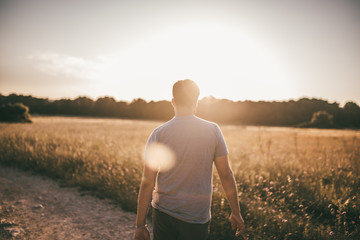 Mann wandert durch ein Feld im Sommer im Gegenlicht