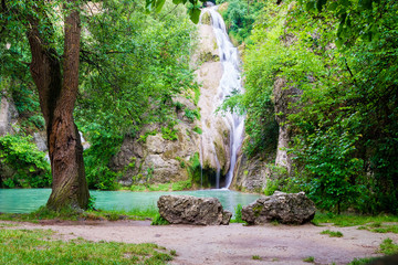 Kaya Bunar / Hotnitsa waterfalls in Bulgaria. Scenic view of the falls with two big rocks and an old tree in front. Picturesque, authentic, eco spot for tourists visiting eastern Europe.