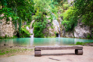 The Hotnitsa Falls (Kaya Bunar) in Bulgaria, with turquoise waters, a bench, and green, luxurious vegetation grown everywhere. Authentic, natural, touristic spot in eastern Europe.