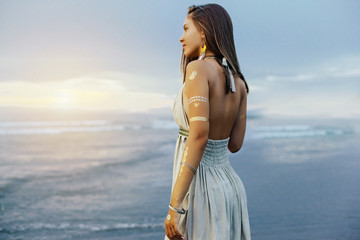Young girl with silver tattoo and boho jewelry on sunset