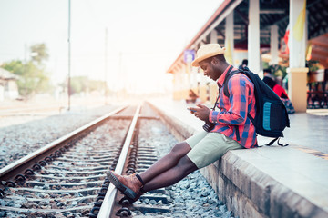 Fototapeta premium African man traveler playing smartphone waiting for the train on railroad station