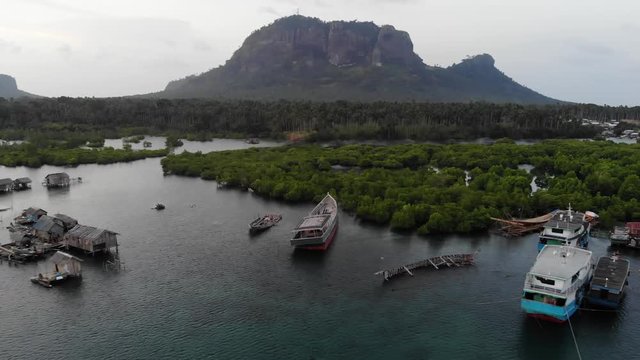 Drone ascending and backing from boats moored near homes on stilts in a peaceful bay near mangroves in Tawi Tawi, the Philippines. Sunset view of a small village on the water.
