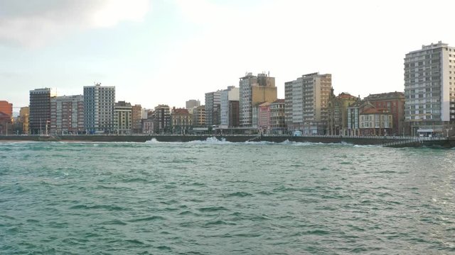 The skyline of the city of Gijon (Asturias, Spain). High buildings facing the sea, waves moving the water. Clouds creating an even lighting.