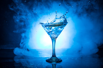 Martini cocktail glass in hand splashing on dark toned smoky background or colorful cocktail in glass with splashes and olives. Party club entertainment. Mixed light. Selective focus