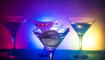 Martini cocktail glass in hand splashing on dark toned smoky background or colorful cocktail in glass with splashes and olives. Party club entertainment. Mixed light. Selective focus