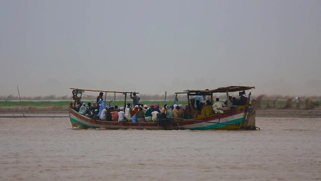 Huge group of Asian Pakistani people with ladies and motor bikes travelling on boat over a river, People under the shelter of the boat