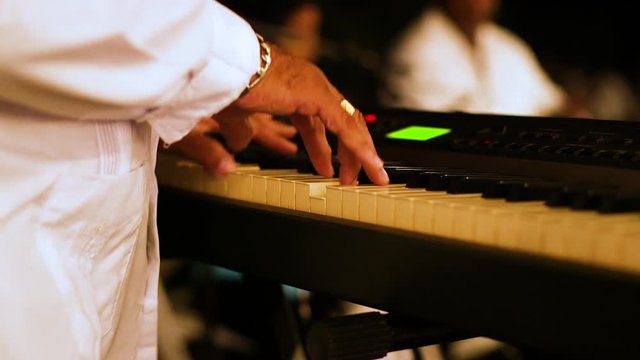 Close up shot of adult male playing the keyboard at a concert at night