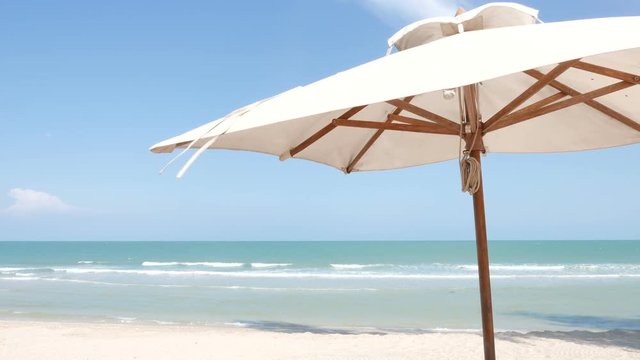 White fabric sun umbrellas parasol close-up from below with blue sky on the background. Ocean view & sandy beach with room for text copy.