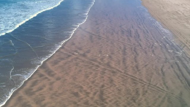 Revealing drone shot of incoming waves on a long beach with dunes on the rigth side