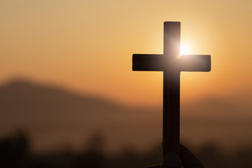 Silhouette of young woman hands holding  lift of christian cross with light sunset background.