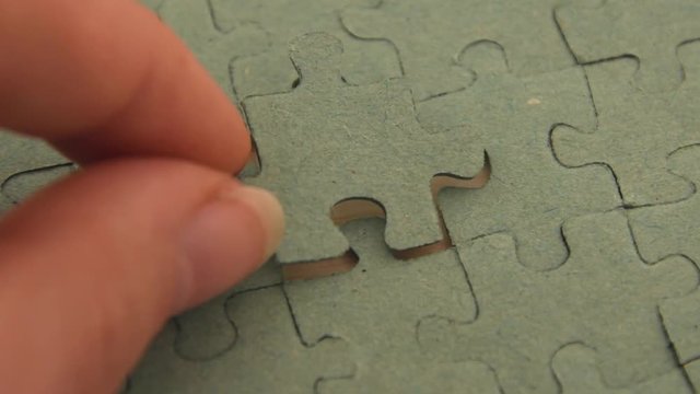 Close up of a young girl's hand putting a puzzle piece in the last blank spot concluding a single color puzzle, on a light wooden background