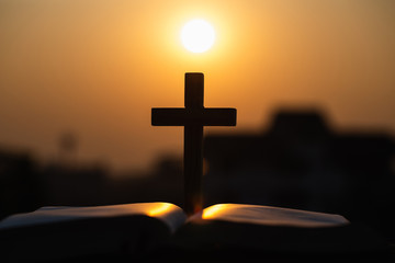 Silhouette of  wooden Christian cross on bible with a bright sunrise as background , god.