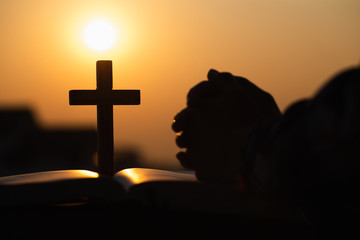 Silhouette of christian young woman praying with a  cross and open the bible at sunrise, Christian...