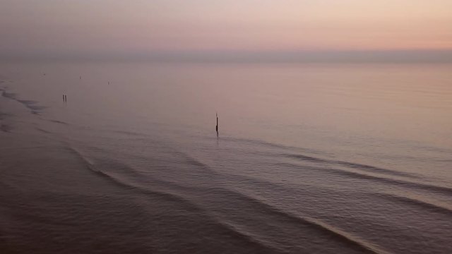 Aerial shot of a calm Northsea beach during sunset. Shot with a drone, moving shots. Low to high shot with a tilt down.