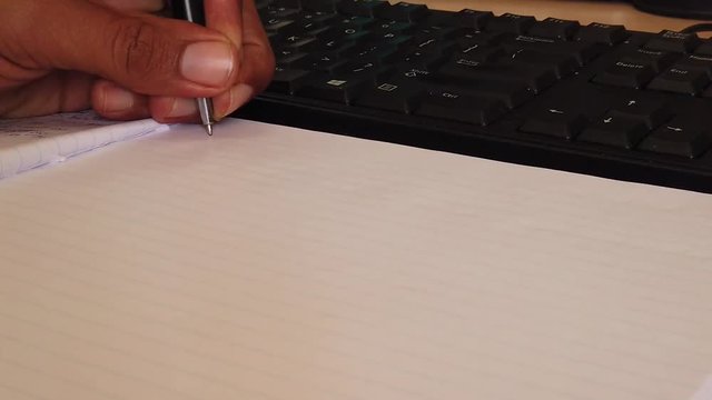 Writing down the notes on a notebook on the desk next to the key board as background.