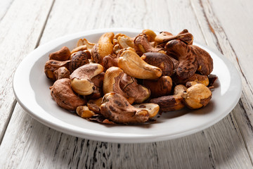 side view cashew nuts on a dish on white wood background