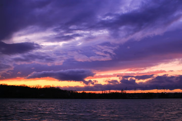 Naklejka na ściany i meble Dark sky above the water had gray and colorful clouds. Sunset at the approach of a rainstorm