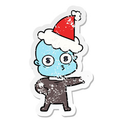 distressed sticker cartoon of a weird bald spaceman wearing santa hat