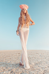 Beautiful young girl wearing native indian headdress with pink feathers and a white mesh dress on the beach