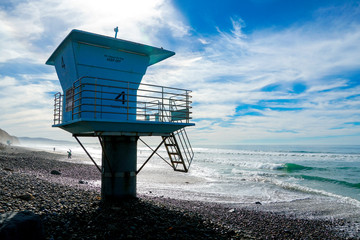 Blue lifeguard tower on a rocky sand beach with clouded blue sky sunny end of day, on Torrey Pines State Beach in California, located in San Diego County.