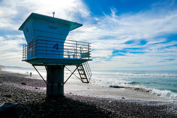 Blue lifeguard tower on a rocky sand beach with clouded blue sky sunny end of day, on Torrey Pines State Beach in California, located in San Diego County.