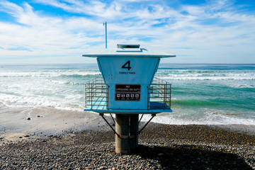 Blue lifeguard tower on a rocky sand beach with clouded blue sky sunny end of day, on Torrey Pines State Beach in California, located in San Diego County.