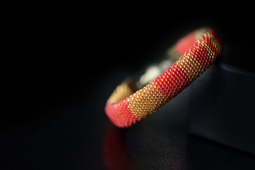 Bead crochet bracelet red and yellow color on a dark background close up