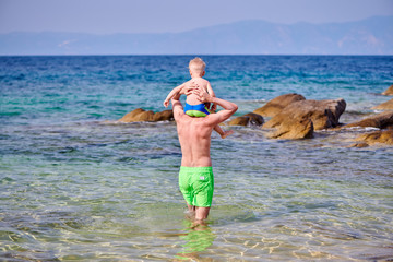 Toddler boy on father's shoulders at beach