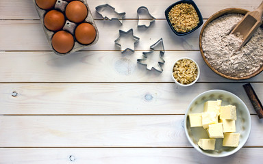 Culinary background with ingredients for baking. Oatmeal, sugar, eggs, butter, cinnamon sticks, nuts, cookie cutters made of metal on a wooden white background,  Flat lay, top view