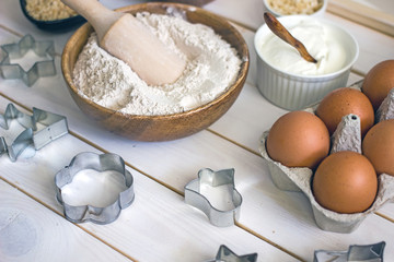 Оat flour in a wooden bowl with a spoon in the middle of the table, next to baking ingredients and forms for cookies. Culinary background