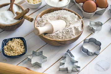 Оat flour in a wooden bowl with a spoon in the middle of the table, next to baking ingredients and forms for cookies. Culinary background