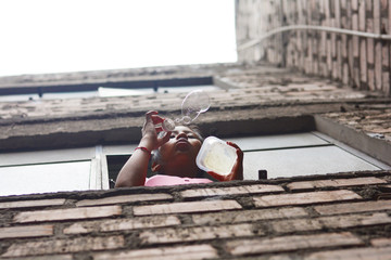 Native american teenager girl blowing soap bubbles from the window of brick building.