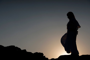 Fototapeta na wymiar A woman silhouette is standing on a top of rock with twilight sky in an evening