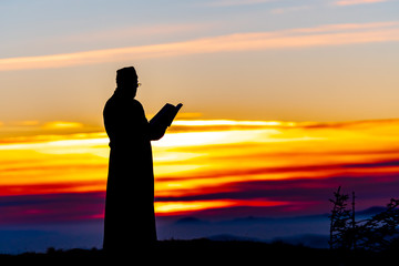Fototapeta premium Priest silhoute reading in the sunset light, Romania