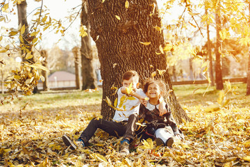 little beautiful dark-skinned girl sitting in the autumn park with her European little friend