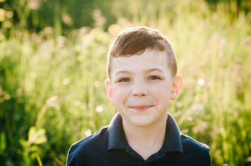 Portrait of a handsome little guy, boy on the background of green and yellow grass in the nature. Happy face is close. Sunlight is summer.