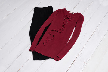 Clothes and accessories. Black midi skirt and red sweater with lacing on white wooden floor planks. Flat lay