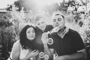 The son and parents on grass and blowing soap bubbles in sunlight summer park. Happy family in the...