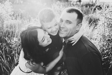 Happy young family spending time together outside in nature on vacation outdoors. Mom, dad and son sit in the grass. The concept of family holiday. Black and white photo.