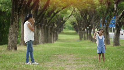 Asian family, mother and daughter doing string phone play activities tie rope at the park.