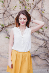 Summer portrait of young beautiful woman in a white blouse and yellow skirt near stone wall with ivy. 