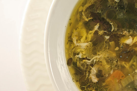 Vegetable and orache soup with egg white on a white bowl and plate.