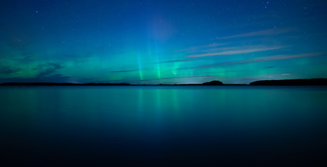 Fototapeta na wymiar Northern lights dancing over calm lake after the sunset under the blu time