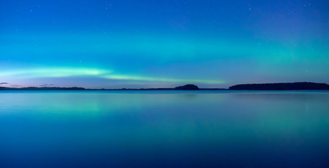 Naklejka na ściany i meble Northern lights dancing over calm lake after the sunset under the blu time